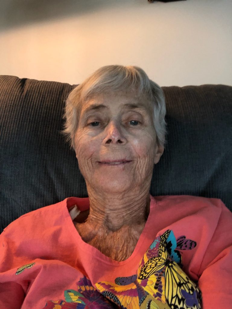 Gray-haired woman in salmon pink shirt.